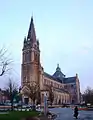 Vue d'ensemble d'une grande église avec un clocher-porche monumental, une nef à trois vaisseaux étagés, un transept surmonté d'une tour-lanterne