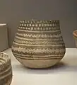 Vase sans col en argile peint de différents motifs géométriques noirs et rouges pâle.