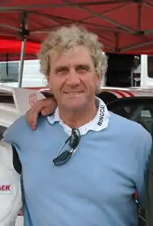 Un homme en pull-over bleu avec des lunettes de soleil accrochées à son col.