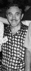 photo en noir et blanc en plan rapproché taille, d'un homme d'une soixantaine d'années, souriant.