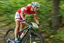 Femme vététiste en compétition, en pleine forêt, maillot et cuissard rouges; arrière-plan complètement flou