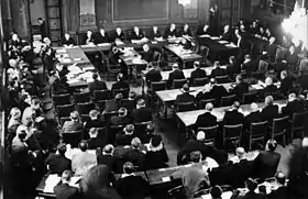 Le Procès en responsabilité de guerre en novembre 1945. Les membres du tribunal sont derrière la table en forme de fer à cheval, devant eux les secrétaires et les sténographes, derrière en trois rangées les accusés et leurs avocats. À gauche, le procureur, les représentants de la Commission de contrôle et des diplomates étrangers, au premier plan le public et les journalistesSoini 1956, p.&nbsp;181.
