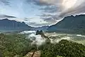 Pitons karstiques, brume et nuages colorés au lever du soleil, vus du sommet du mont Nam Xay (côté nord), pendant la mousson, à Vang Vieng. Juin 2020.