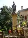 Statue de l'Immaculée Conception. Sur le socle sont représentés : une ancre (symbole de l’espérance, l'une des trois vertus théologales), le monogramme marial composé des lettres A et M entrelacées, initiales de l’Ave Maria, et le Cœur Immaculé de Marie