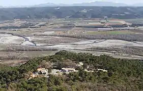 Hameau de pavillons modernes, au milieu des chênes verts, sur un promontoire dominant la vallée de la Durance, plate et découpée de champs carrés. Au fond, le plateau de Valensole ondulé et sombre.