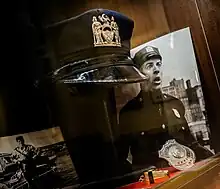 Casquette et insigne de la police de New York arborés par Ludovic Cruchot dans Le Gendarme à New York.