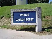Photographie d'un panneau de rue avec des écritures blanches sur fond bleu.