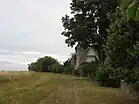 Photographie en couleurs d'un champs bordé par des haies et la clôture d'un manoir