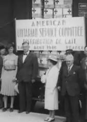 photo noir et blanc d'un groupe de personnes devant un wagon de marchandises contenant des cartons de lait