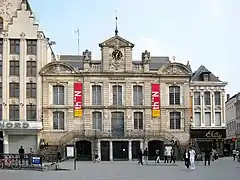 Photo du Théâtre du Nord, de part et d'autre du bâtiment se trouve un escalier permettant d’accéder au premier étage. Une horloge surplombe le bâtiment au centre.