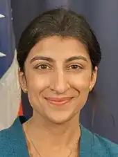 Photo en buste d'une femme souriante, aux cheveux noirs et attachés, portant un haut bleu et un collier.