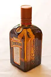 Photographie d'une bouteille de Cointreau, rectangulaire et de couleur orangée, vue de trois-quarts avant.