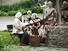 Des artisanes en costume d'époque réalisent des ceintures fléchées à l'extérieur.