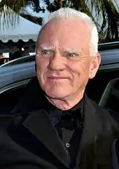 Un homme aux yeux bleus et aux cheveux blancs ayant à peu près 70 ans, souriant