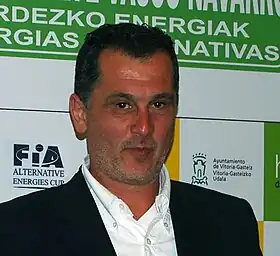 Photographie d'un homme brun, vu de face, habbilé dans un costume, vu en gros plan.