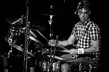 Photographie en noir et blanc d'un batteur lors d'un concert.