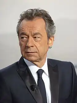 Photo de face de Michel Denisot portant un micro à sa bouche.