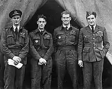 Photographie noir et blanc de quatre hommes, debout, de face, en uniforme de pilote.