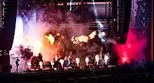 Quatre membres d'un groupe de rock jouant sur une scène avec des effets pyrotechniques
