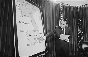 Nixon se tient devant une grande carte de l'Indochine et montre le Cambodge du doigt.