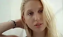 Photographie d'une jeune femme blonde, la main dans les cheveux.