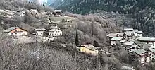 Photographie de bâtiments plus ou moins uniformes avec des lauzes ou de la tôle grise au toit ainsi que des murs en pierres, blancs ou encore en bois, répartis en différents groupements dans la montagne.