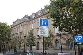 Cliché numérique couleur. Partie de façade d'un bâtiment de quatre étages avec au moins sept ouvertures encadrant la porte centrale.