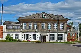 Photographie d'un immeuble en bois à deux étages, avec le rez-de-chaussée en brique blanche et l'étage en bois marron.