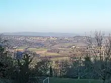 Au premier plan, le stade communal dans l’ombre ; puis les champs en contrebas ; puis des collines avec une agglomération (Reillanne) ; tout au fond, la masse sombre de la montagne de Lure.