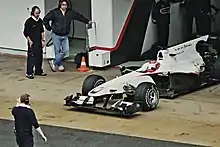 Photographie d'une monoplace blanche sortant des stands, vue de haut, de trois-quarts