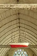 Vue en contreplongée d'une maquette blanc et rouge suspendue par des chaînes à une poutre.