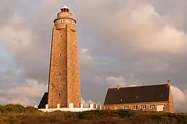 Photographie en couleurs prise d'assez près vers un phare bordé par un bâtiment.