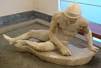 Statue. Un homme nu est assis sur le sol et s'appuie sur sa jambe.