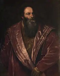 Image - buste d'un personnage en noir et blanc, portant une ample coiffe arrondie vers le haut, regard fixe, barbe longue bouclée tombant sur le col arrondi d'une sorte de cape.