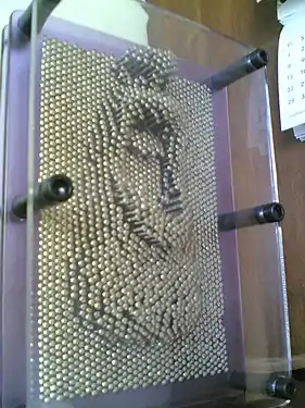 Un Pin Art de taille standard, avec en relief la moitié inférieure d'un visage.