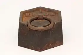 Un poids d'un kilogramme de qualité domestique en fonte grise. Sa forme suit la recommandation R52 de l'OIML pour les poids hexagonaux en fonte grise.
