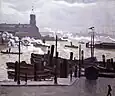 Peinture dans les tons gris représentant des bateaux sombres amarrés sur un quai et d'autres sur l'eau crachant de la fumée blanches ; au fond, quelques bâtiments