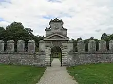 Grand mur crénelé, avec une porte en bossage surmontée d'un blason