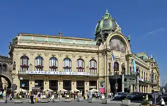 Un grand édifice Art nouveau, de couleur claire, au toit de cuivre et au corps central surmonté d'une grande fresque et d'un dôme.
