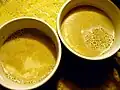 Deux verres de mélange de pinol dans du lait chaud, mélangés de manière presque homogène. Les restes de poudre de pinole flottent à la surface du lait.