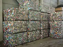 Dans un grand hall en béton gris, une quinzaine d’énormes parallélépipèdes rectangles forment comme un haut mur ; chacun est formé de centaines de boîtes de conserve compressées.