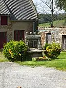 Photographie en couleurs d'un puits en pierre dans un hameau.