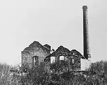 Deux bâtiments en ruine sans toiture et une grande cheminée.