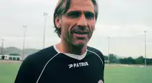 Photographie d'un homme blond, aux cheveux mi-court, avec un t-shirt noir de marque Patrick.