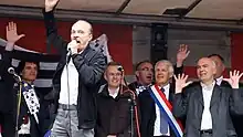 Photographie d'Alan Stivell au micro sur scène devant les élus bretons
