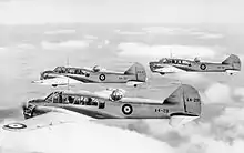 Photographie noir et blanc de trois avions dans le ciel, vu de côté, à la même altitude.