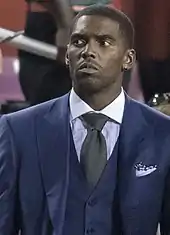 Un homme en costume bleu foncé regarde suspicieusement sur le côté.