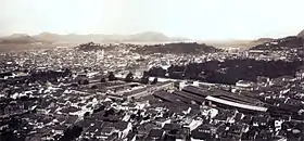 Vue plongeante sur les toits d'une grande ville avec des collines et un cours d'eau dans le lointain
