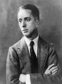 Photographie en noir et blanc de Norman Rockwell jeune, bras croisés, en costume avec une cravate sombre et une chemise blanche