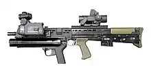 photographie en couleur montrant de profil un fusil d’assaut avec plusieurs modules fixés autour et sous le canon.
